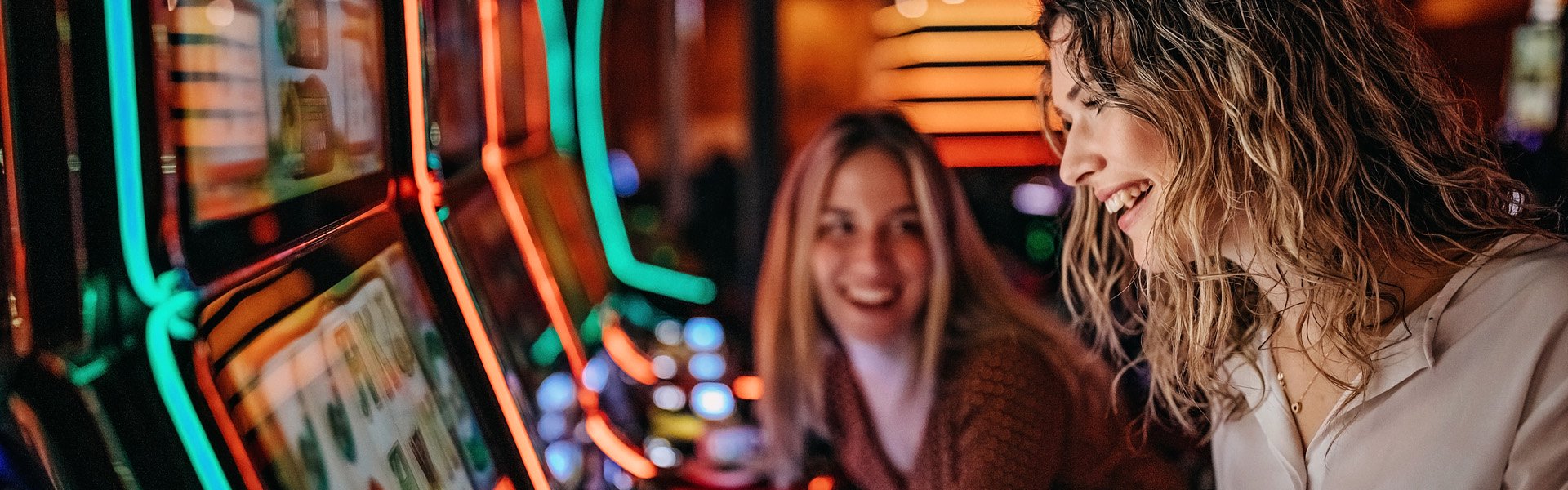 Two guests playing brightly lit slot machines inside Happy Valley Casino in State College, Pennsylvania.