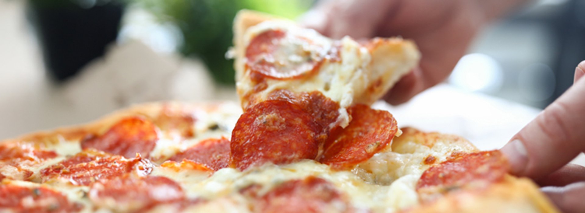Hands grabbing a slice of pepperoni pizza