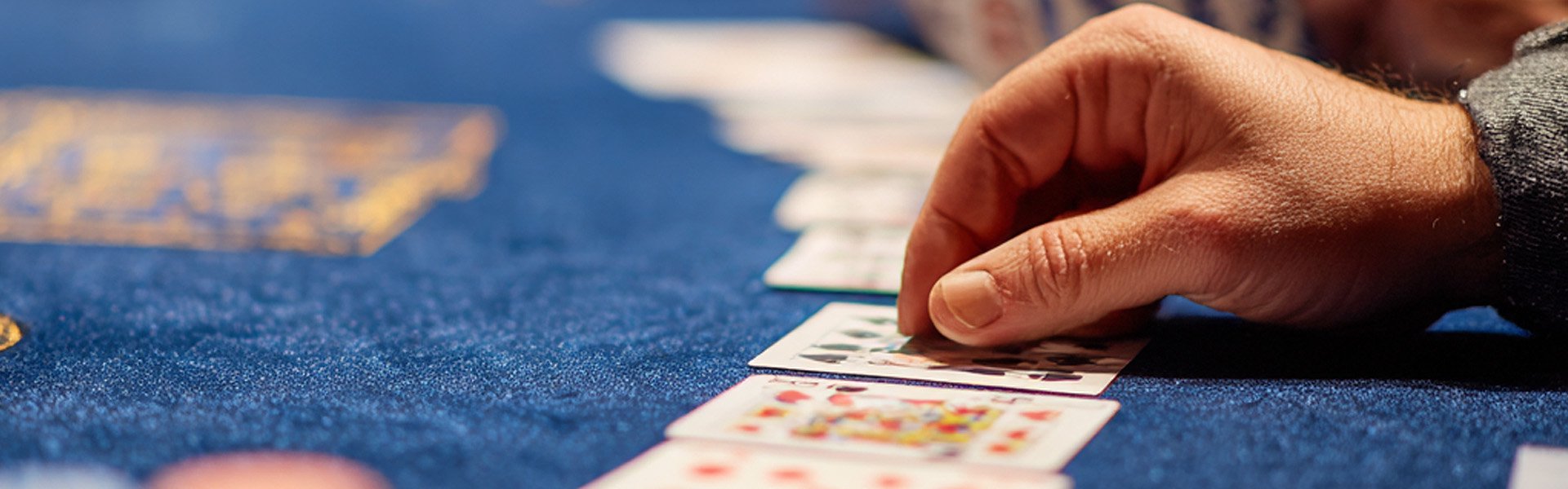 Hand arranging playing cards on a blue casino table at Happy Valley Casino in State College, Pennsylvania.